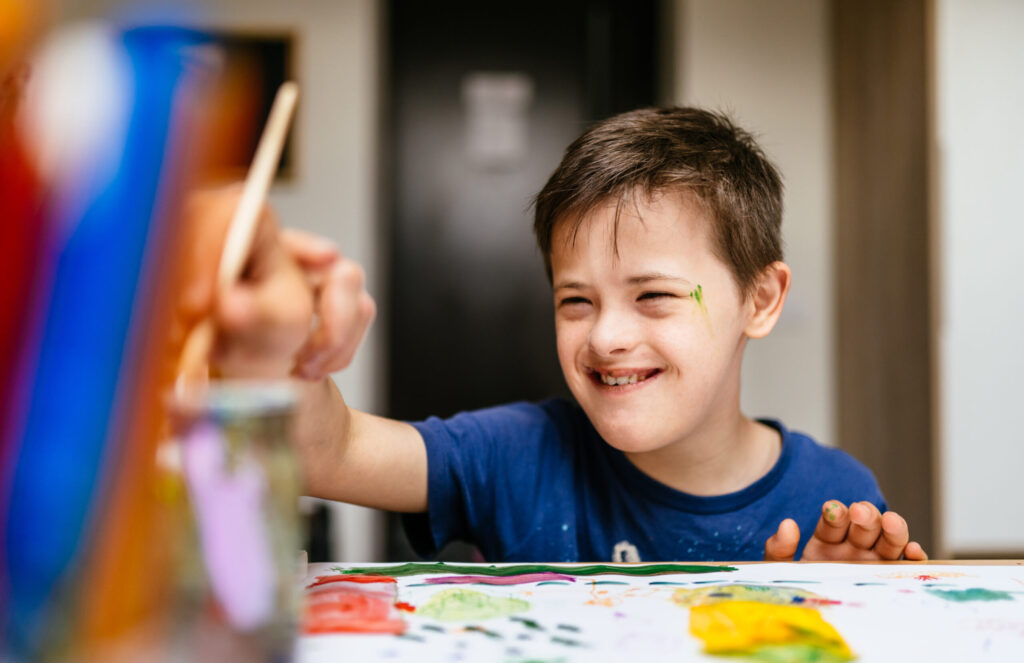 Young Caucasian Boy with Down Syndrome Concentrating picking up colors on the table to paint a picture at art class studio.